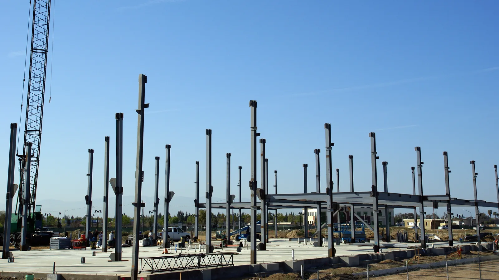Steel columns rising from a concrete slab at a low-rise commercial construction site with a crane