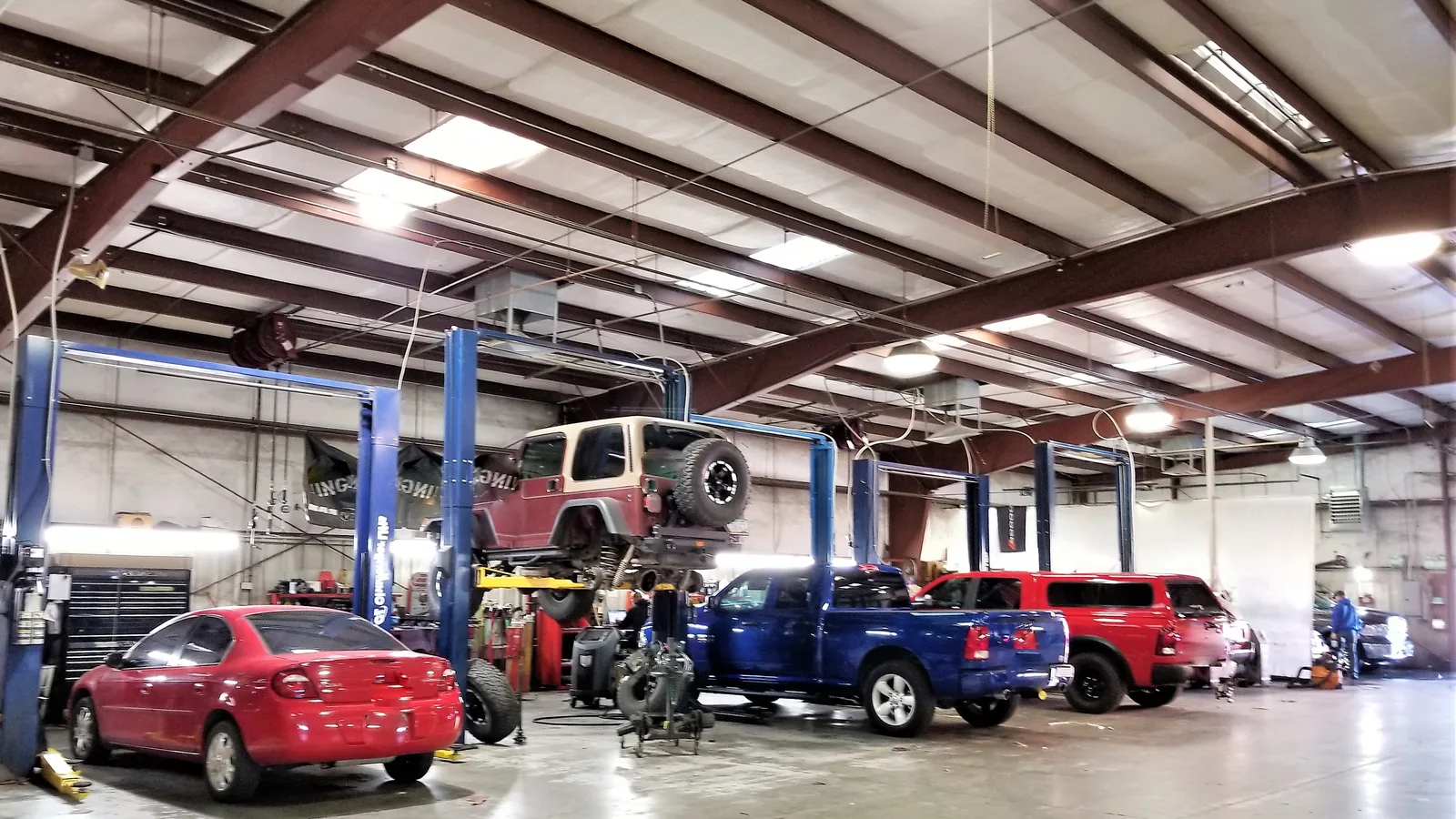 Cars and pickup trucks raised on lifts inside a busy auto service shop