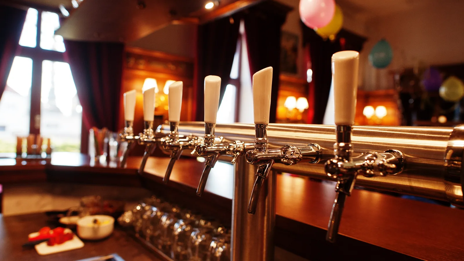A row of polished beer taps along a bar, with glasses lined up beneath