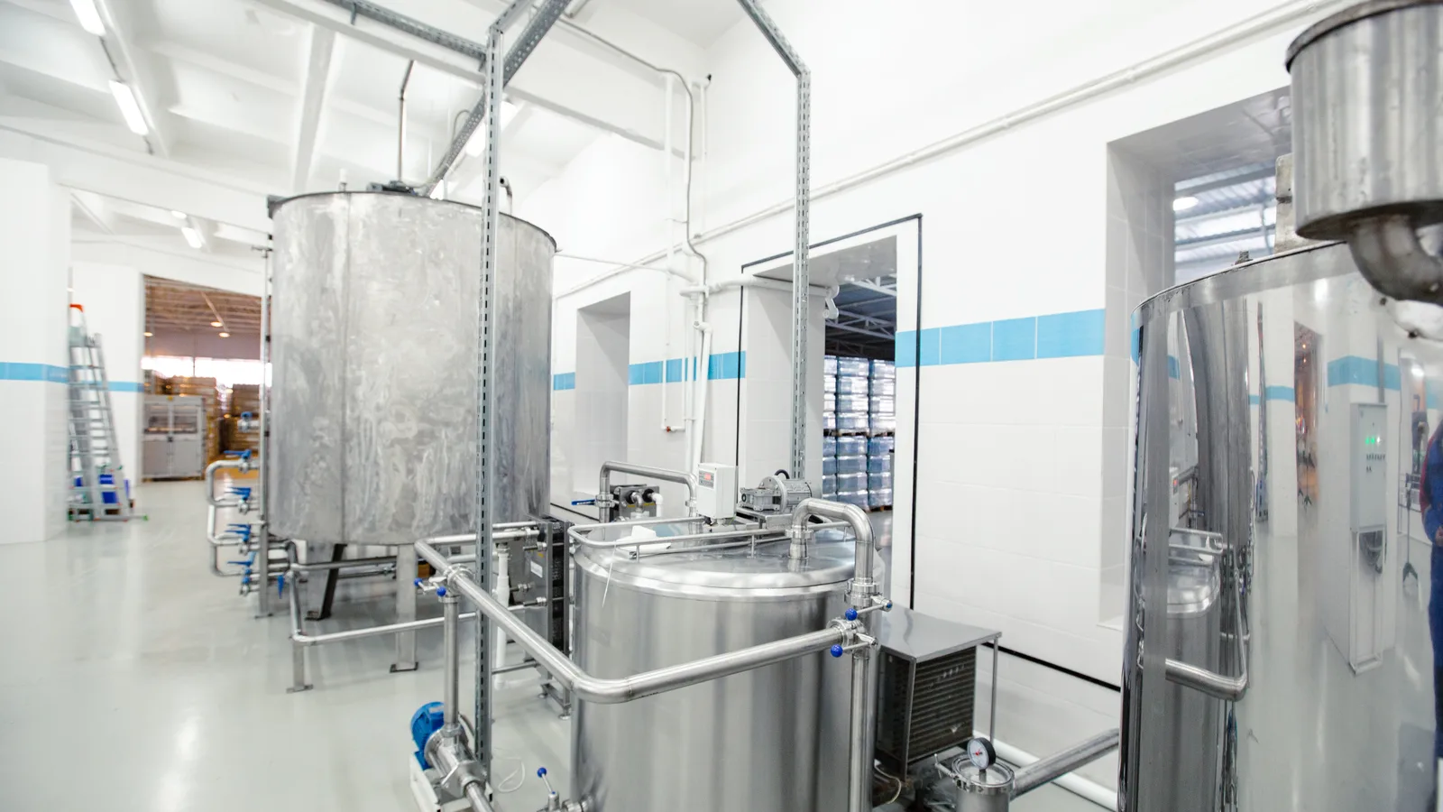 Stainless steel mixing tanks and piping inside a clean, empty food processing room