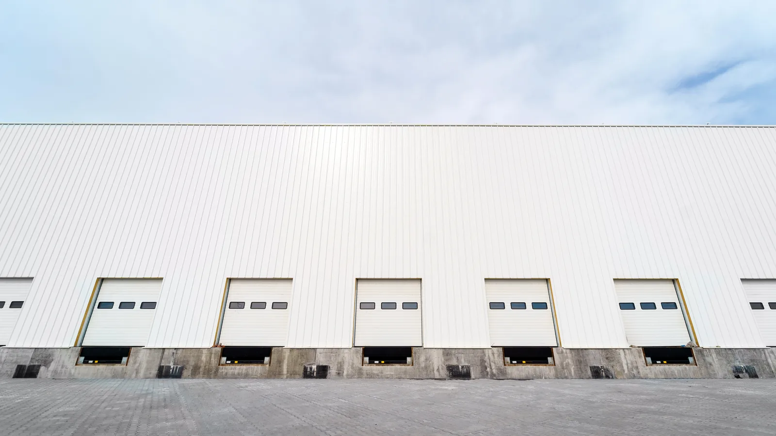 A row of loading dock doors along the side of a long white metal industrial building