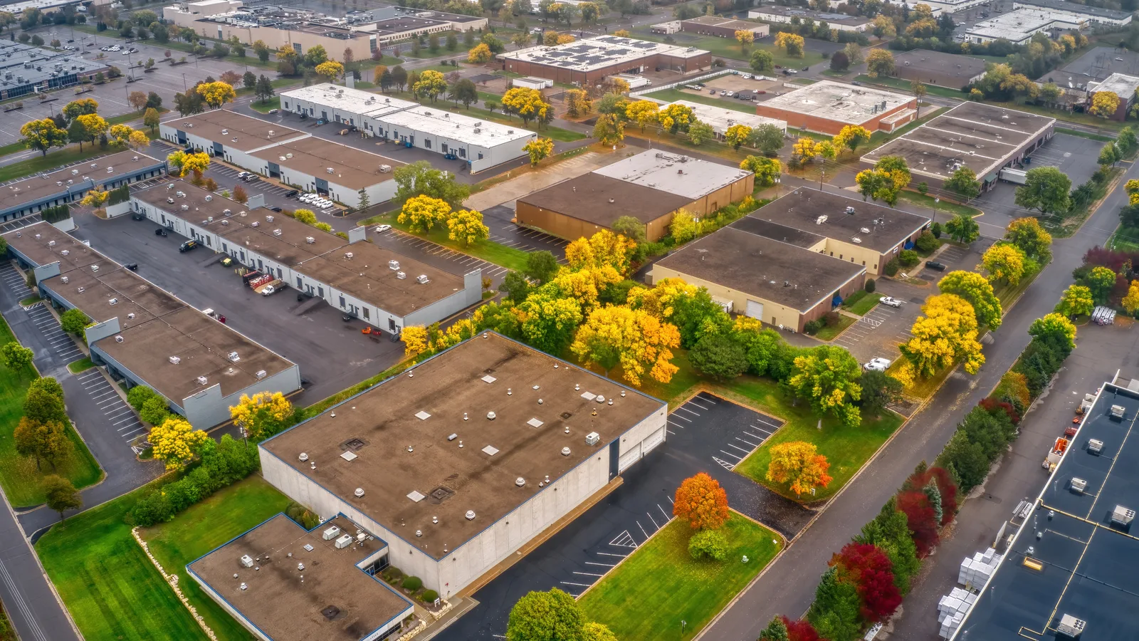 Aerial view of low industrial and office buildings with parking lots among trees in autumn color
