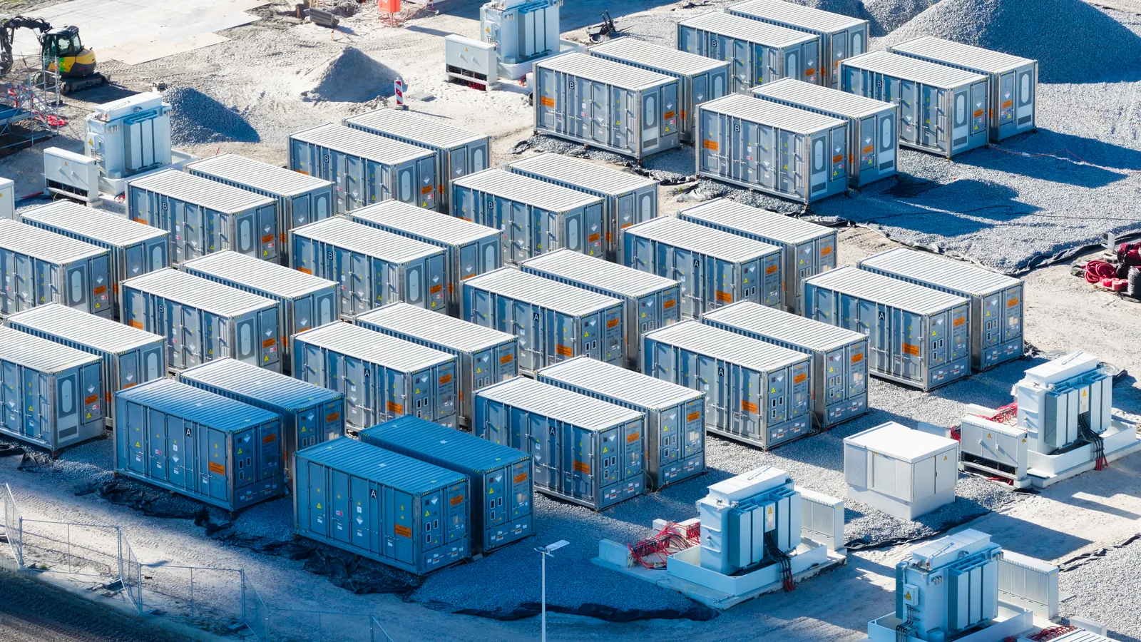 Aerial view of rows of battery storage containers and transformers on a gravel utility site