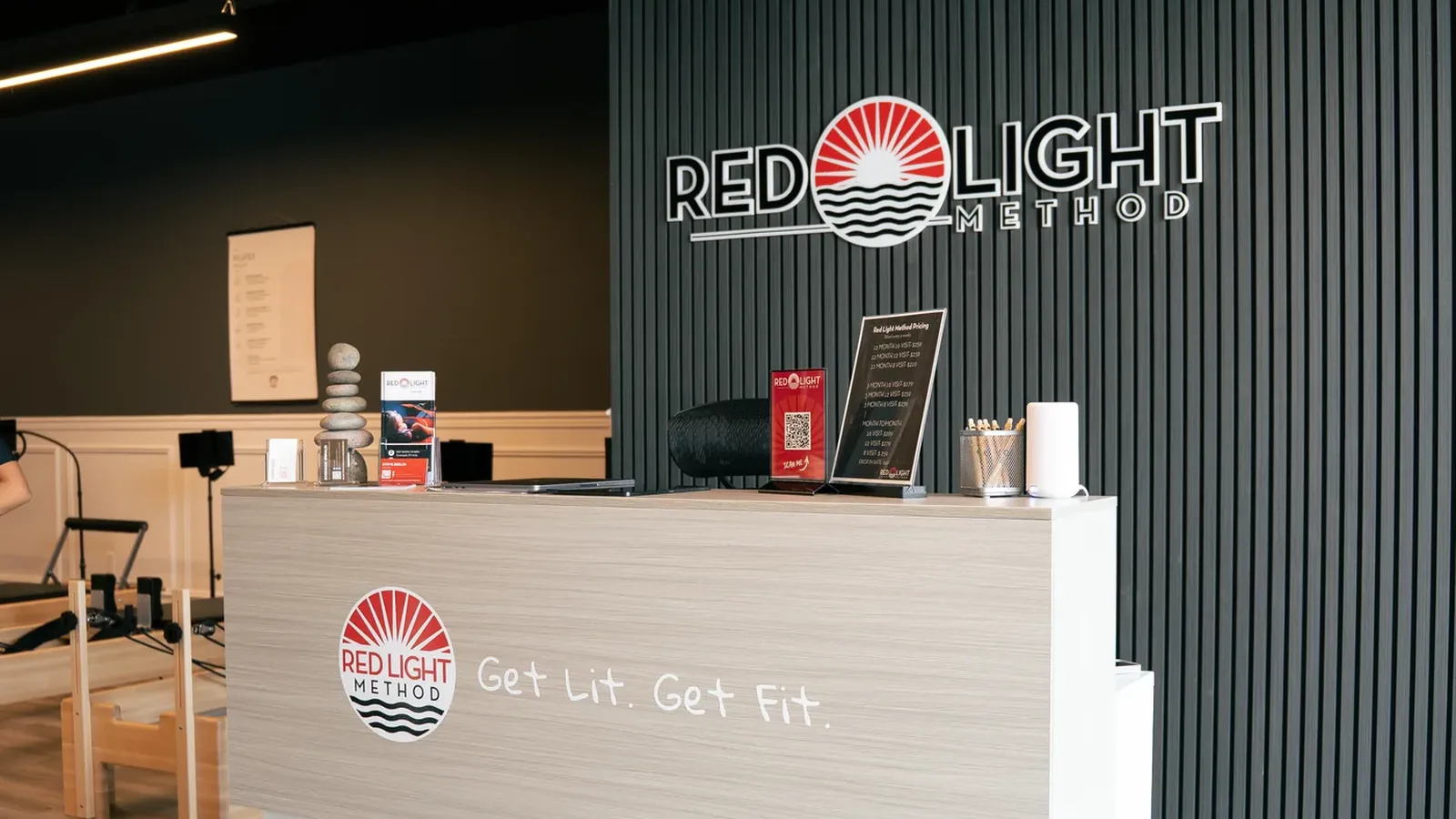 The front desk at Red Light Method Commack, with the studio's Get Lit. Get Fit. line on the counter and the Red Light Method sign on the wall behind it