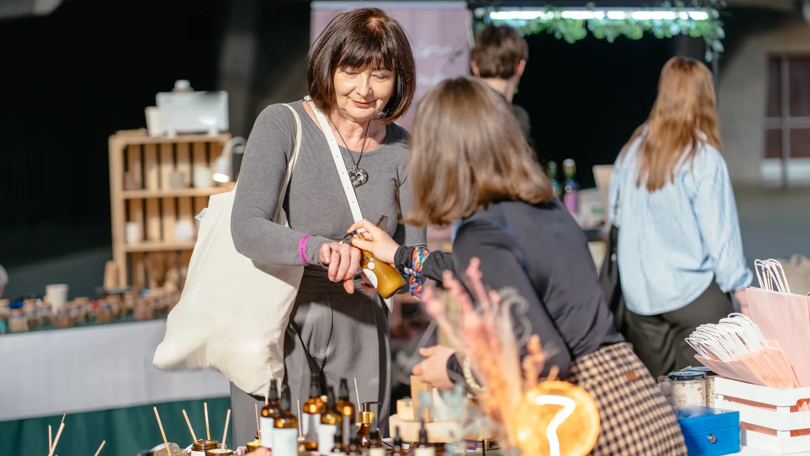 A shopper tests a skincare product held out by a vendor at a busy market table