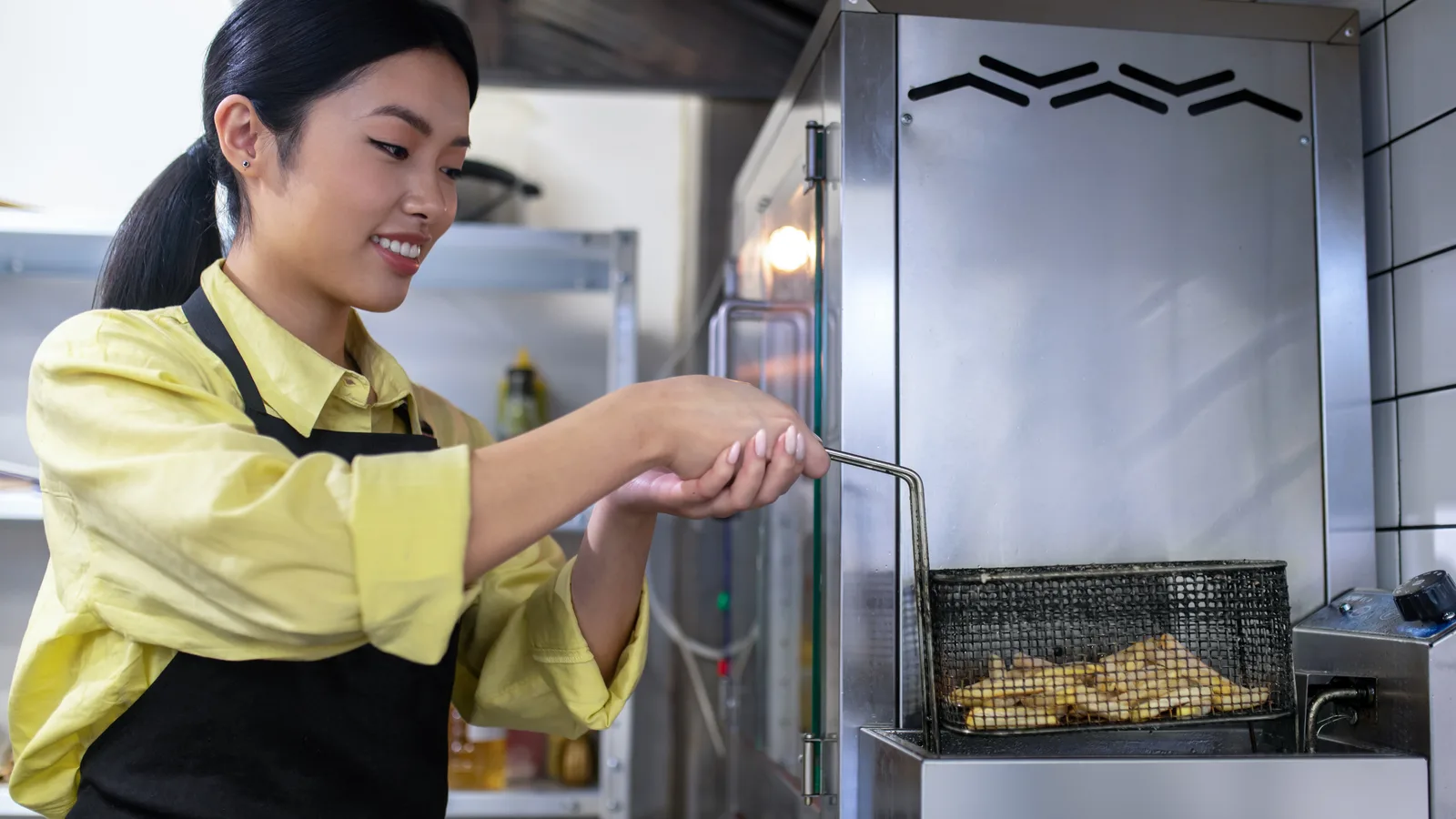 A restaurant worker lowering a basket of fries into a commercial fryer
